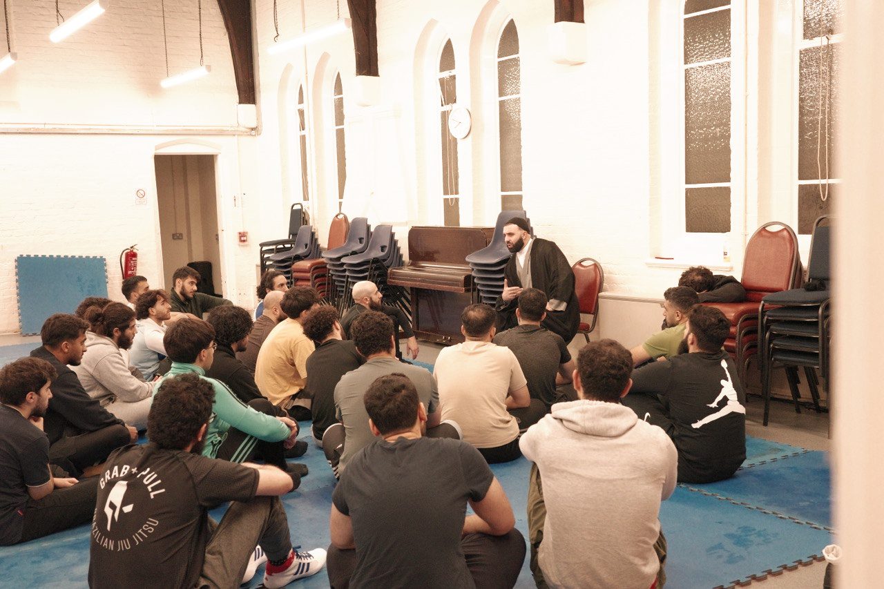 Members sitting on the mats listening to a talk before training begins.