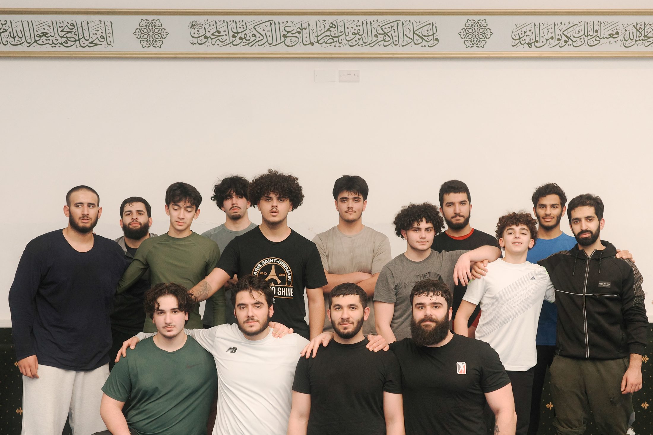 The Badr Grappling squad lined up together in the hall, beneath a band of Arabic calligraphy running along the wall.