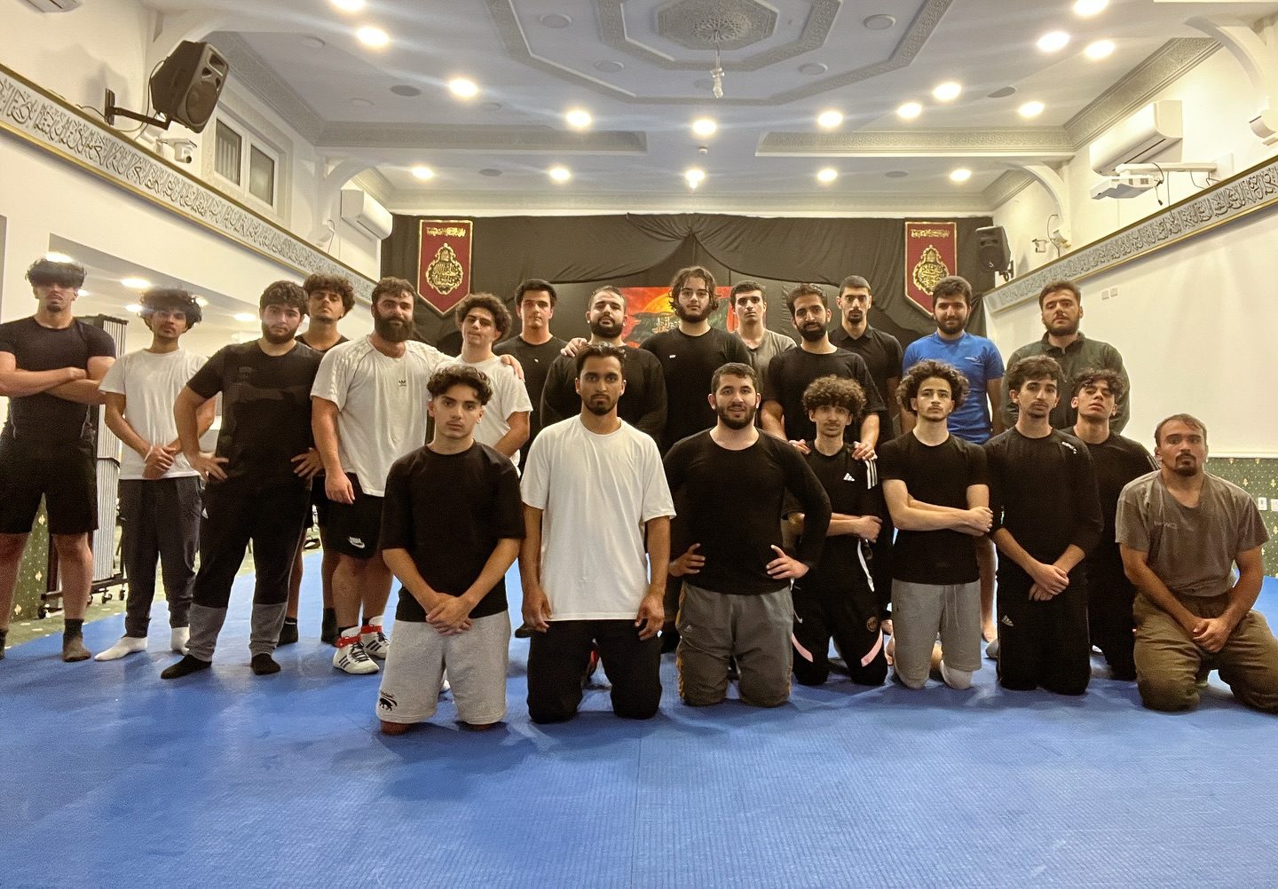 Members standing and kneeling in two rows on the blue mats at the end of a session.